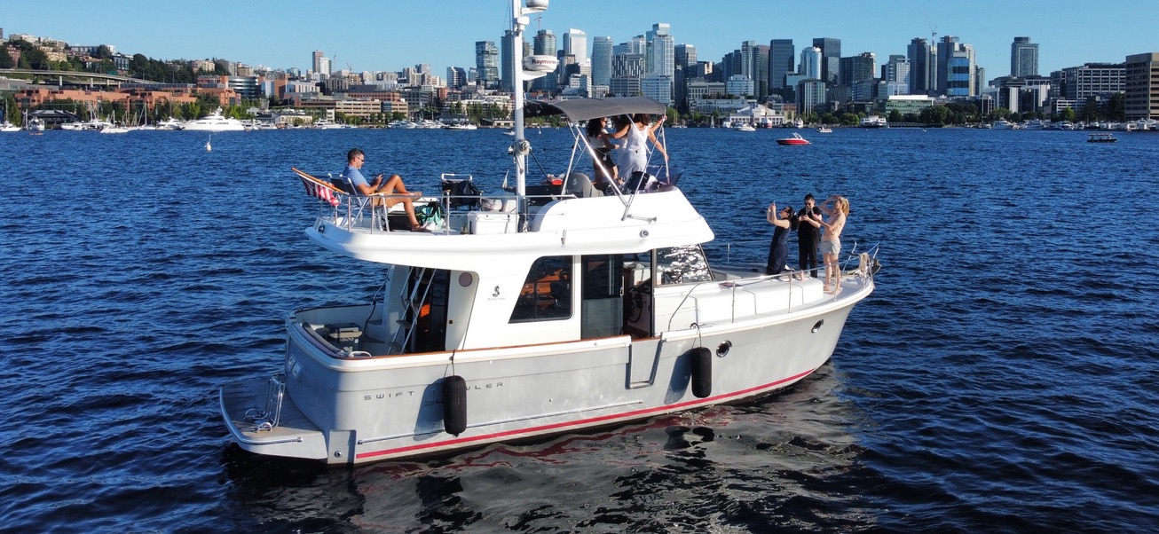 The charter yacht cruising in front of the Seattle skyline with guests on the bow and flybridge
